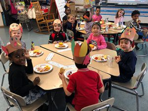 picture group of kindergarten students seated at cluster of desks eating food