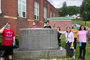 picture of students and teacher standing next to dirty memorial preparing to clean it