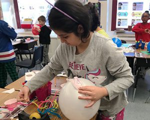picture of student attaching pink yarn "hair" to white balloon