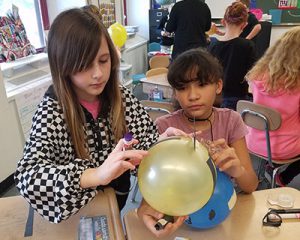 picture of two students gluing stripes of black construction paper on yellow parade balloon