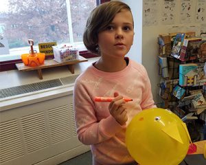 picture of student drawing on a yellow parade balloon with orange marker