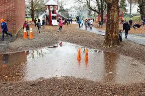 picture of large puddle marked off by orange cones with children playing in the background