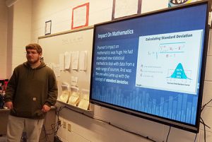 picture of student standing in front of class with presenting a Powerpoint on his statistics research