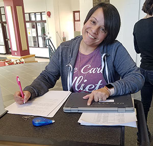 picture of smiling teaching assistant standing at computer cart with Chromebook sign out form