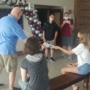 picture of science teacher handing science award scholarship to student seated on bench as high school principal and assistant superintendent take pictures