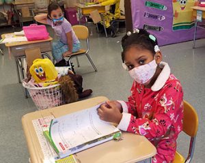 picture of student dressed in pajamas seated at desk opening notebook