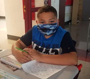 picture of grade 6 student wearing mask, seated at desk holding green pencil 