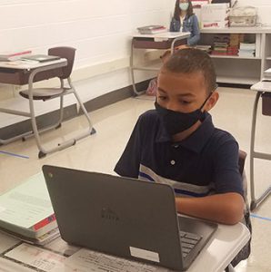 picture of student wearing face mask seated at desk and working on laptop computer