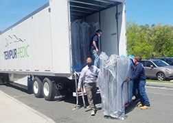 picture of high school principal wheeling cart with mattresses away from the rear door of a tractor trailer