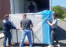 picture of high school maintenance staff loading mattresses onto a cart at the back of a tractor trailer.