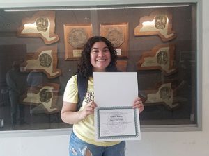 picture of student wearing a mask and holding merit scholarship certificate