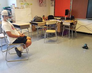 picture of student seated on chair watching robot move across the floor