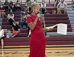 picture of superintendent holding microphone speaking to staff seated on bleachers in high school gym