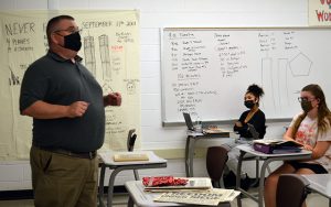 picture of teacher standing near 9-11 wall art speaking to students