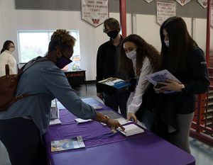 picture of college admission counselor handing out printed brochures to students standing at table.