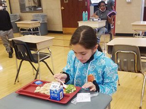 picture of student seated at desk in cafeteria eating lunch