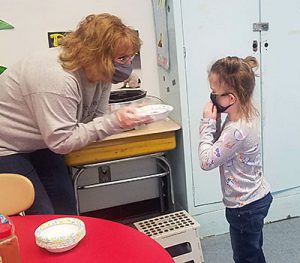 picture of teacher bending down to hand a bowl of applesauce to student