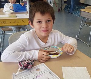 picture of smiling student seated at desk with spoon in a bowl of applesauce