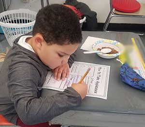 picture of student seated at desk with pencil completing worksheet about steps to making applesauce