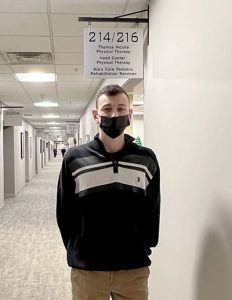 picture of student intern standing in hallway underneath sign outside physical therapy office