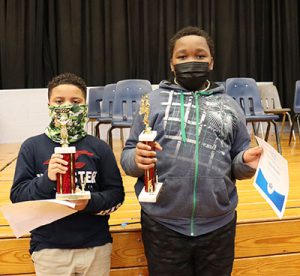 picture of spelling bee winner and runner up holding certificates and trophies