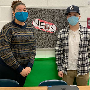 picture of Vliet News announcers standing in front of bulletin board with Vliet News sign and district logo