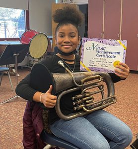 picture of grade 4 Band Student of the Month for January 2022 seated with instrument holding achievement certificate