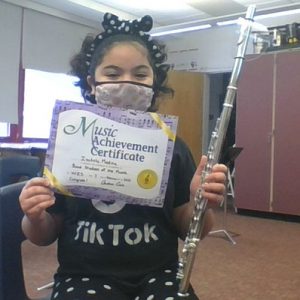 picture of grade 5 Band Student of the Month for January 2022 seated with flute and holding up achievement certificate