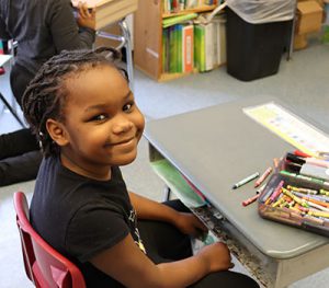 picture of student seated at desk and smiling at camera