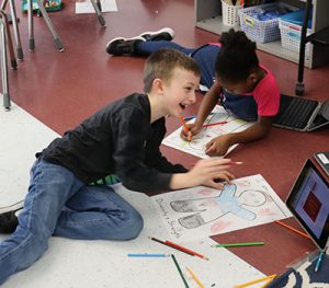 picture of two students on the floor with coloring pencils working on self portraits