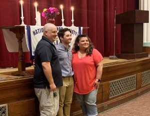 picture of National Honor Society inductee standing next to parents in front of stage with National Honor Society banner and candles representing character, leadership, service and scholarship