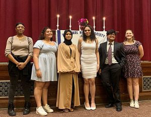 picture of National Honor Society members who presented at the induction ceremony standing in front of stage with National Honor Society banner and candles representing character, leadership, service and scholarship