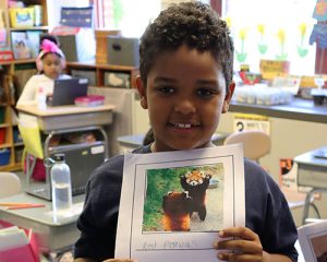 picture of student looking at camera and smiling while holding a picture of a red panda on the cover sheet of a class project