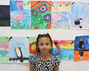 picture of student in a leopard print top standing beneath a portrait of purple and pink flowers she created in art class