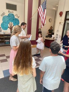 Students and art teacher look on as Elks representative hands out certificates in the school lobby.