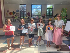 Five students holding certificates for prize winning posters stand in school lobby with their art teachers