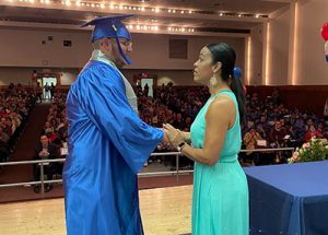 Student in cap ang gown shaking hands with Career and Technical School Principal on stage to receive diploma.