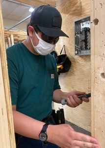 Student in face mask and baseball cap working with electrical wires.