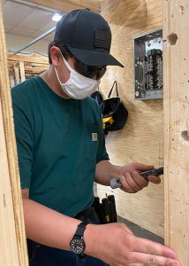 Student in face mask and baseball cap working with electrical wires.