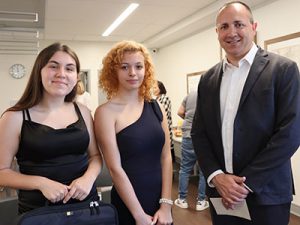 Two students hold black laptop cases in hands while standing beside Watervliet City School District superintendent. All are looking toward the camera and smiling.