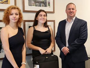 Students holding laptop cases stand next to Watervliet Housing Authority Director Matthew Ethier. All are looking at the camera and smiling.