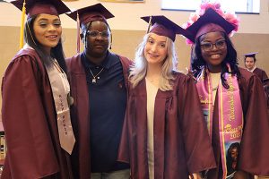 Four graduates stand together smiling at the camera before the ceremony.