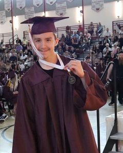 Graduate leaving stage after receiving diploma, looking at camera and smiling.