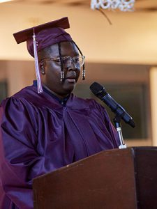 picture of graduation in cap and gown standing at podium speaking into microphone