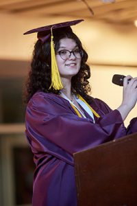 picture of graduation in cap and gown standing at podium speaking into microphone