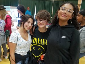 Three students standing together smiling at camera with Career Jam activities in the background.