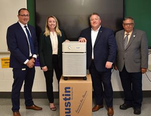 Superintendent Donald Stevens standing with Albany County Executive Dan McCoy, Watervliet Mayor Charles Patricelli and President of Austin Air Systems Lauren McMillan. The four are gathered around an air purifier unit in a Watervliet High School classroom.