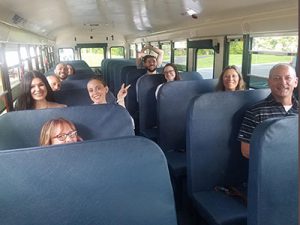 Group of new staff seated in seats on the school bus looking at camera and smiling.