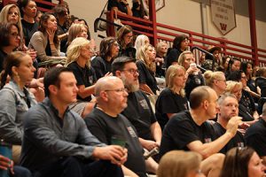 audience dressed mostly in black United in Kindness t-shirts seated on bleachers listening to speaker.