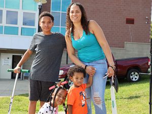 Family stands together looking at camera and smiling on sidewalk leading to athletic field.